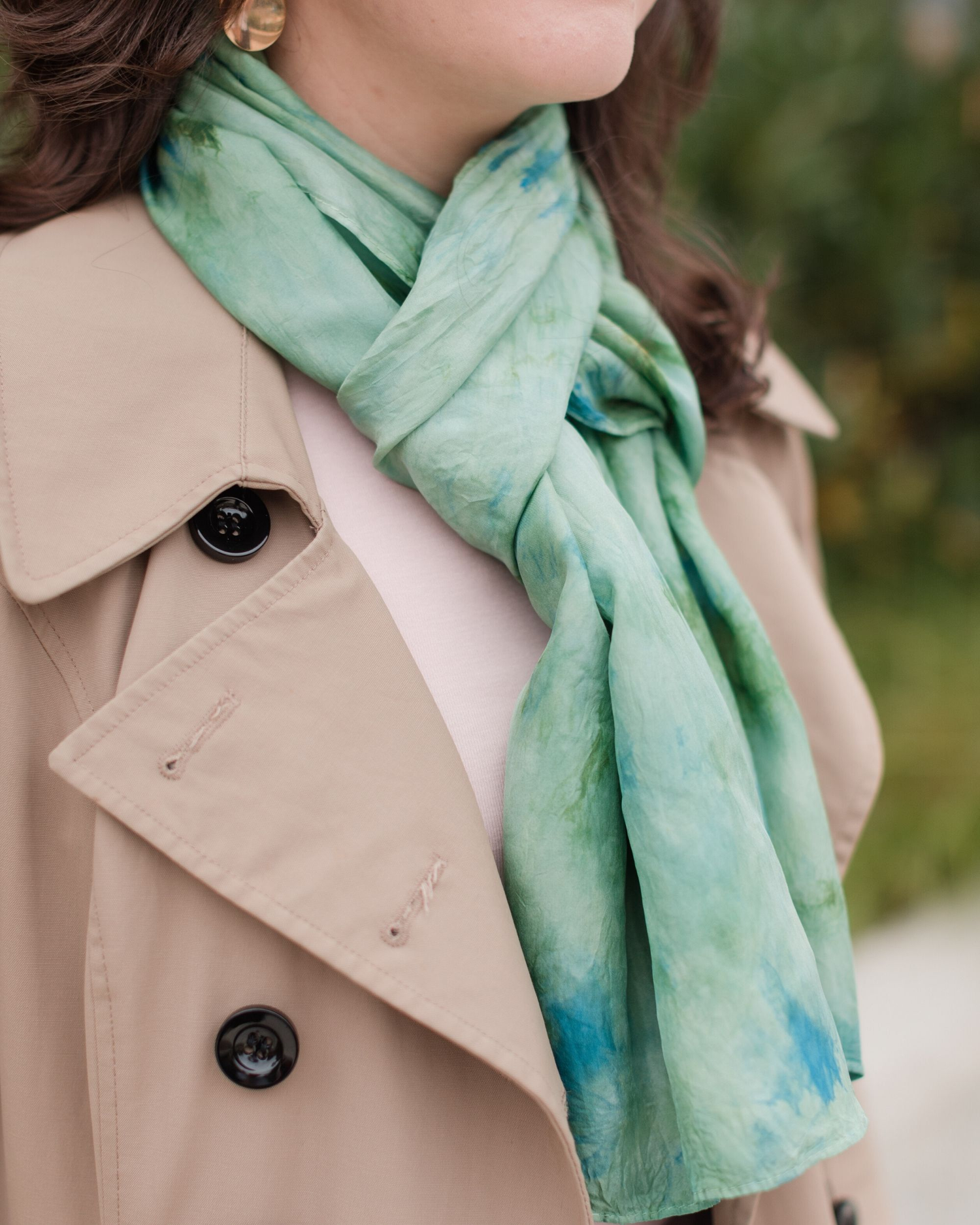 white woman wearing a trench coat, pink shirt & rectangle scarf in juniper