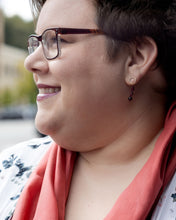 Plus size white woman with pixie cut medium brown hair, glasses, floral open front cardigan, looking off to the side and smiling.  She's wearing delicate garnet drop earrings and a 14x72" russet red silk scarf in a loop around her neck.