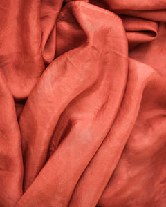 Top down view of russet red silk scarf with gentle folds that create soft highlights and shadows.
